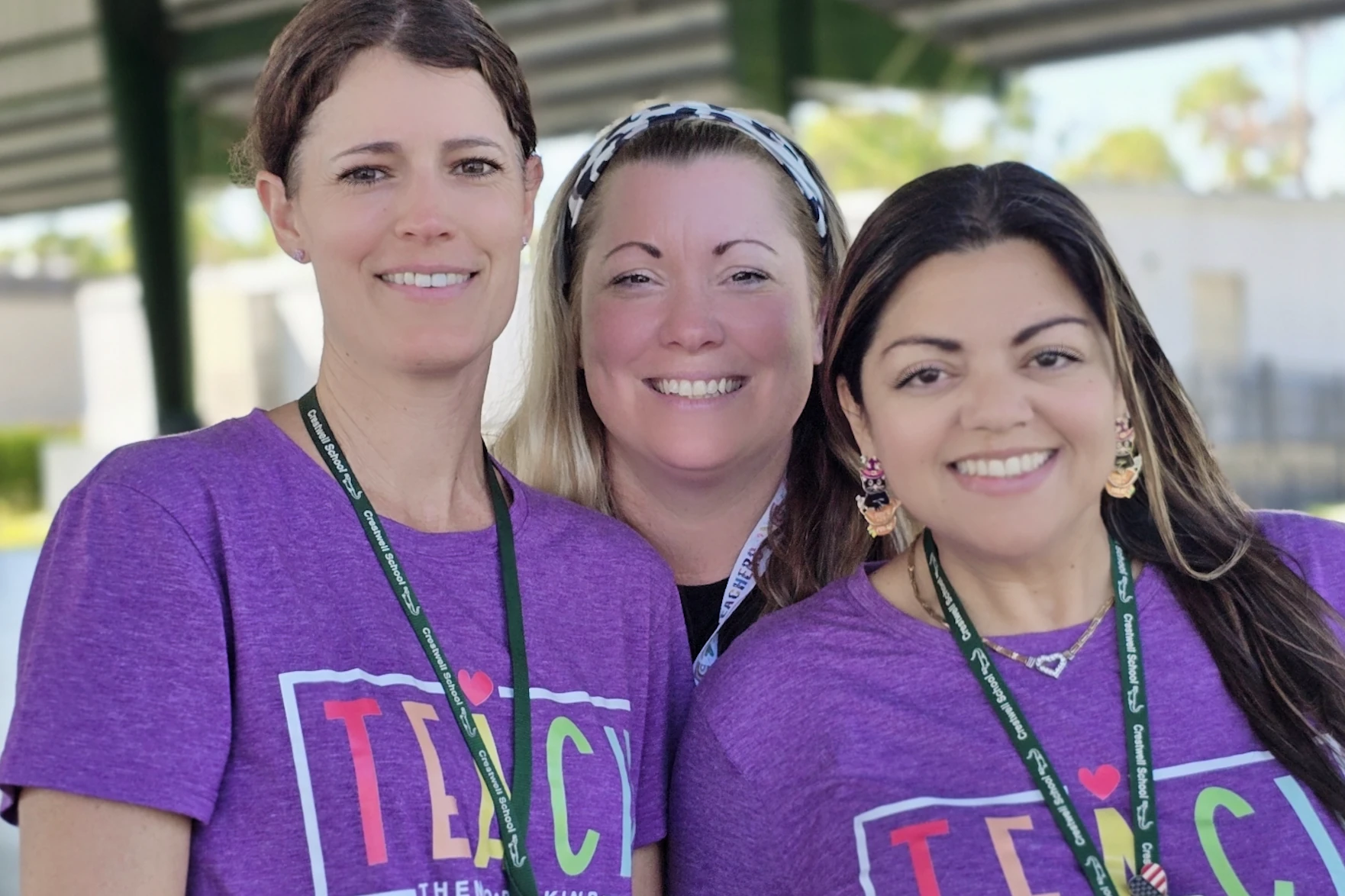Three Crestwell School staff members smiling together under the covered pavilion on campus