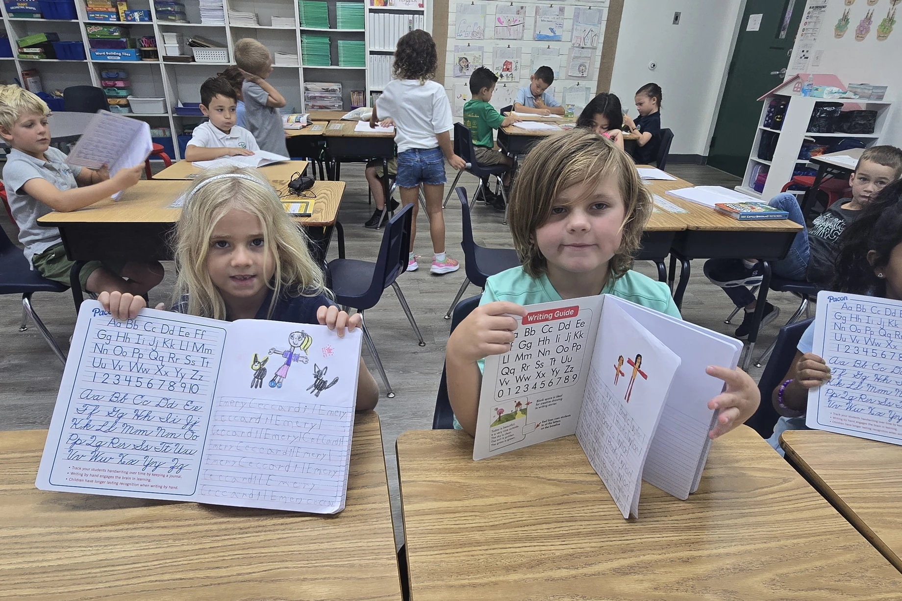 Elementary students at Crestwell School holding up their handwriting notebooks at their classroom desks